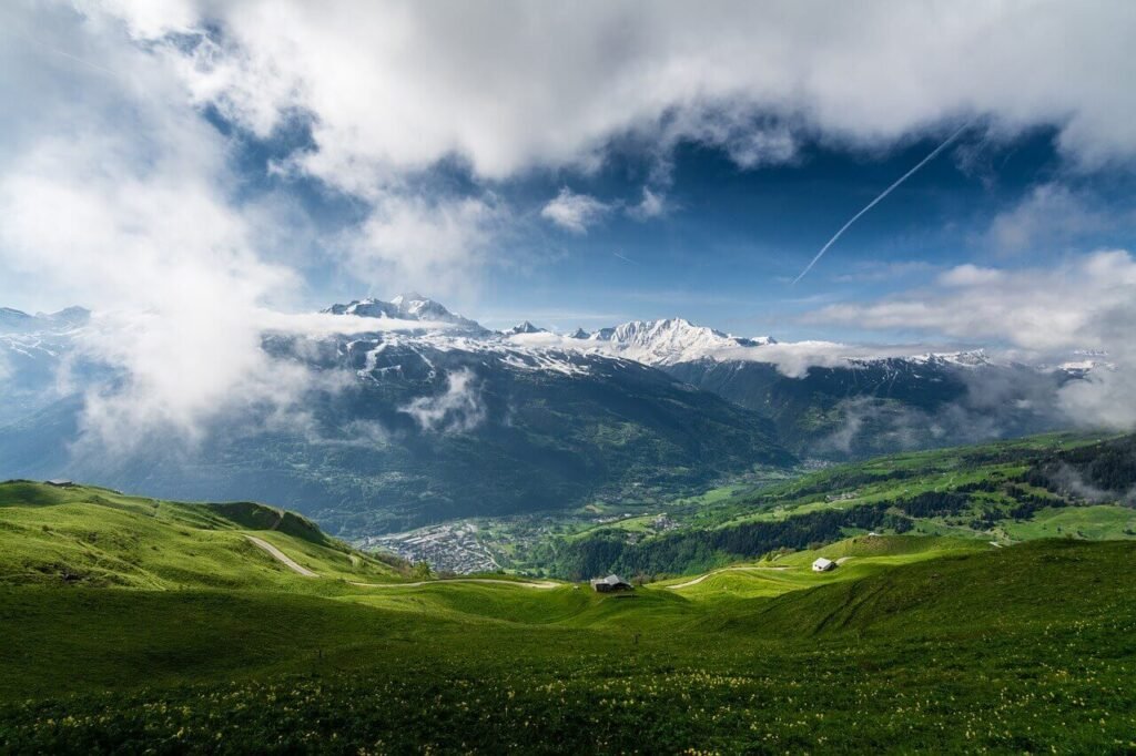 A stretch of green ground leading to distant white hills in a series.Travel to north now